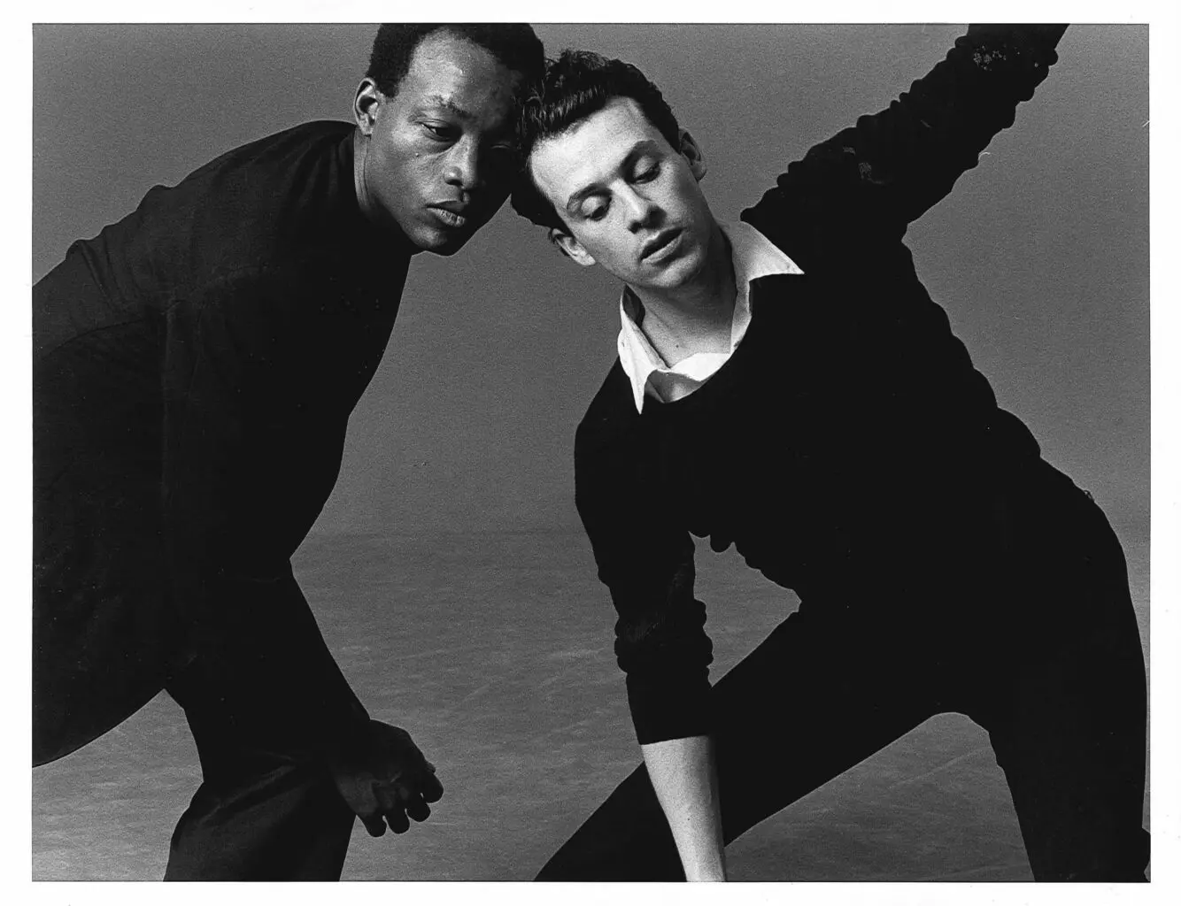 Archival black and white photo of Bill T Jones and Arnie Greenfield. They are in a dyanmic dance pose, with Arnie opening his body towards the camera.