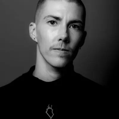 Black and white portrait of s.lumbert. They are wearing a black shirt with a small metal necklace.