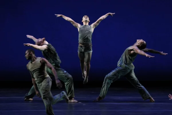 4 dancers wearing black against a dark blue background.