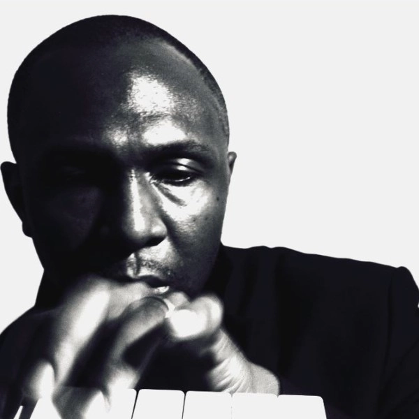 Black and white headshot of HPRIZM. They are playing a small keyboard wearing a black top.