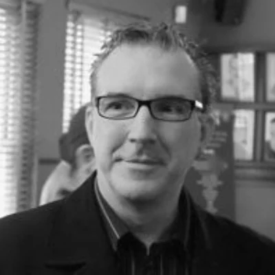 Black and white portrait of Robert Weirzel. They are wearing a black suit, looking past the camera.