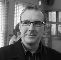 Black and white portrait of Robert Weirzel. They are wearing a black suit, looking past the camera.