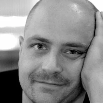 Black and white headshot of Peter Nigrini. They look into the camera with their head resting on their hand.