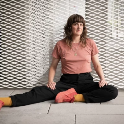 Medium shot of artist Faye Driscoll leaning against a white metal grate wall.
